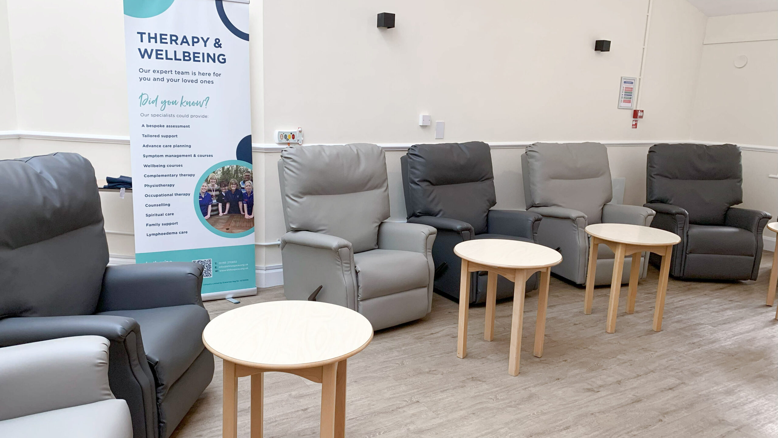 A room with several recliner chairs and small coffee tables, featuring a banner about therapy and wellbeing in the background.