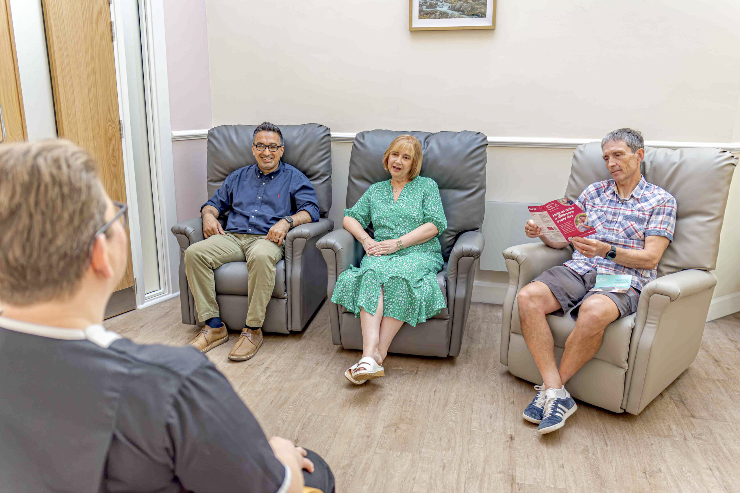 Three people sat in a recliner chair, looking engaged as a therapist sits facing them talking through a session.