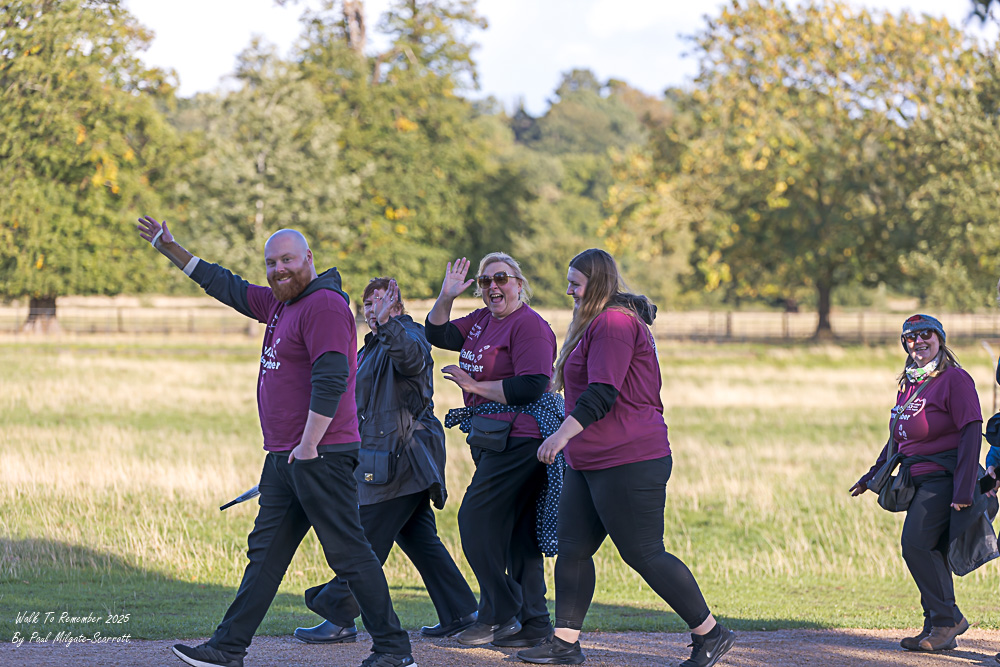 A mixed group of people smiling and waving as they walk.
