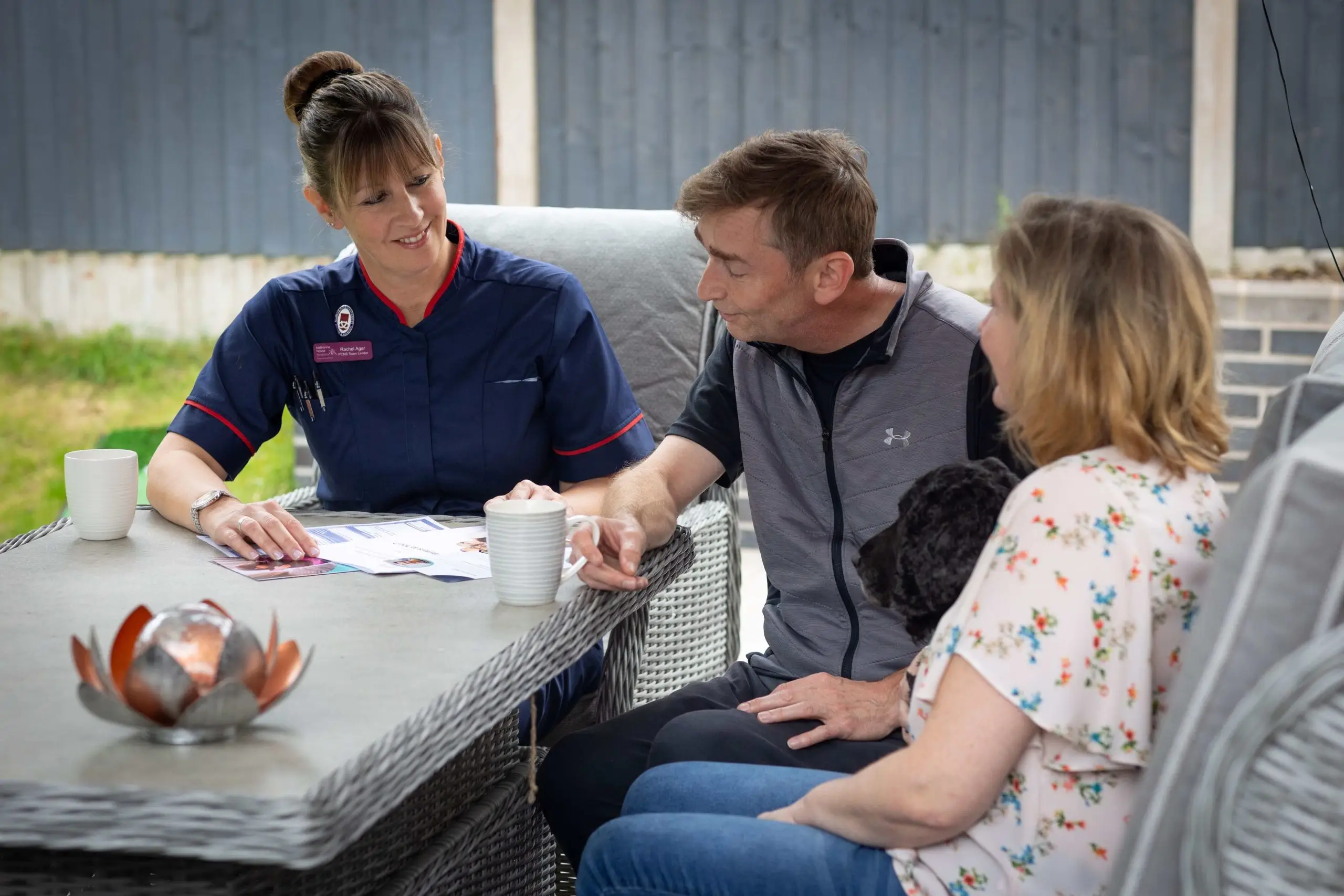 A nurse talks with a family seated at a table in their garden.