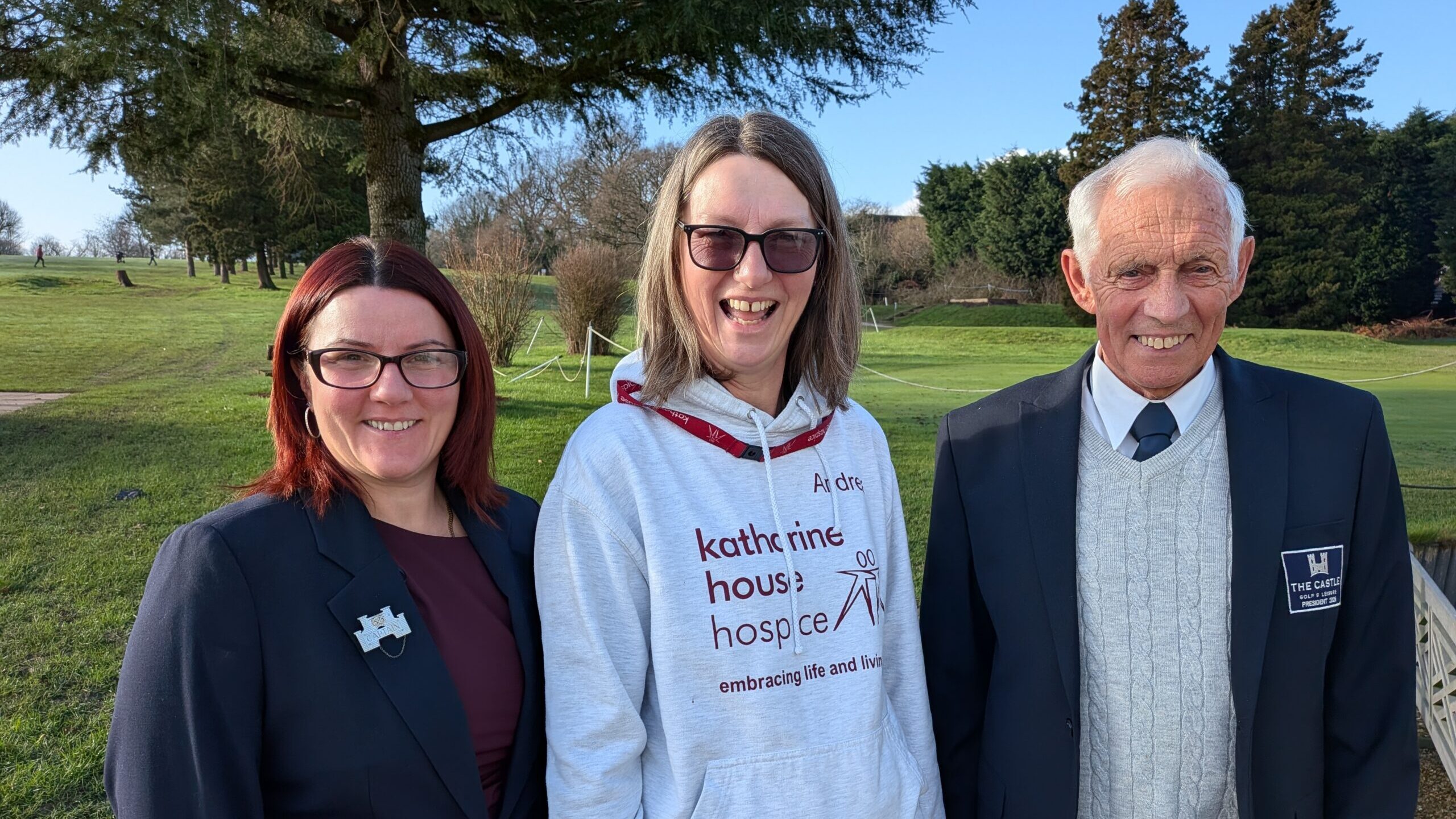 A woman in a Katharine House Hospice hoodie stands between two people in suits.