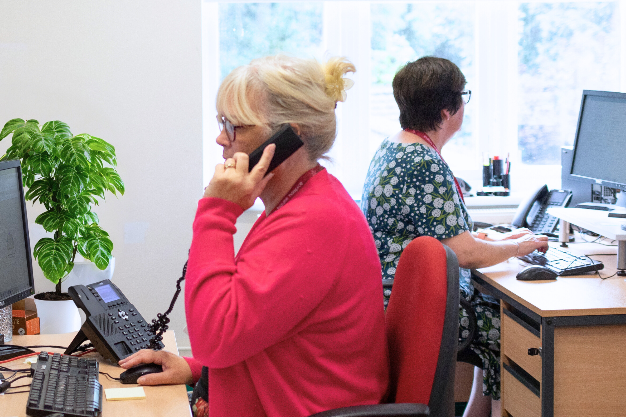 Two people talking on headsets, each sat at a desk.