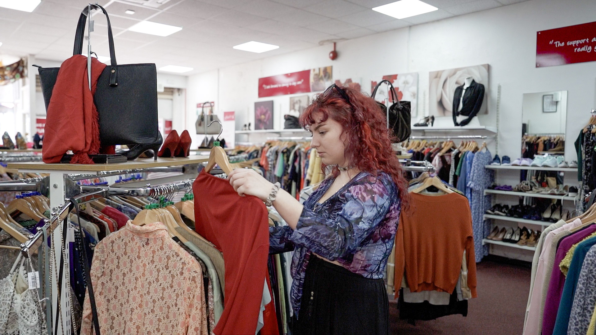 A young woman with red curly hair looking through the clothing section in store.