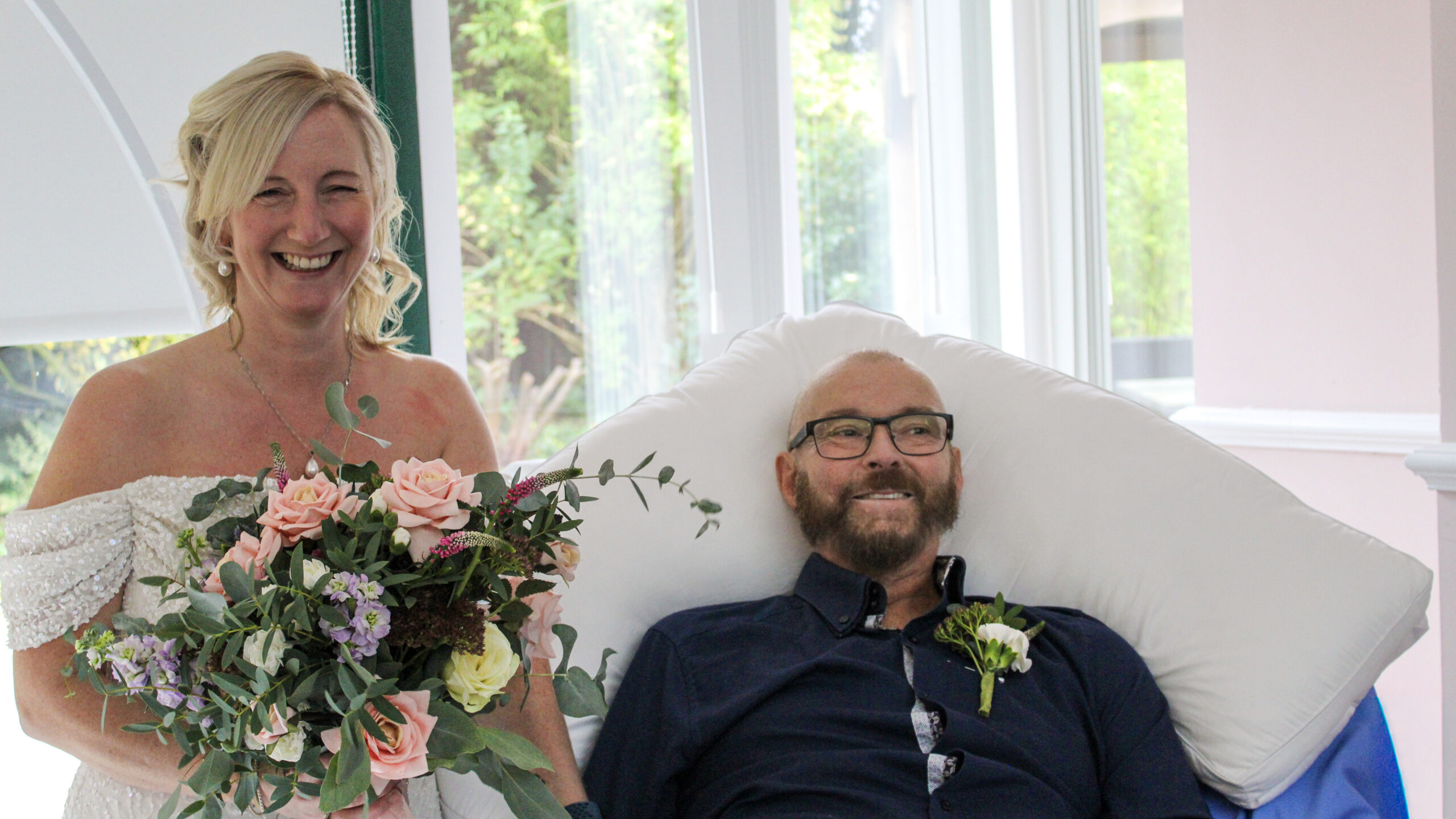 A bride and groom smiling happily after getting married. The groom is in bed.