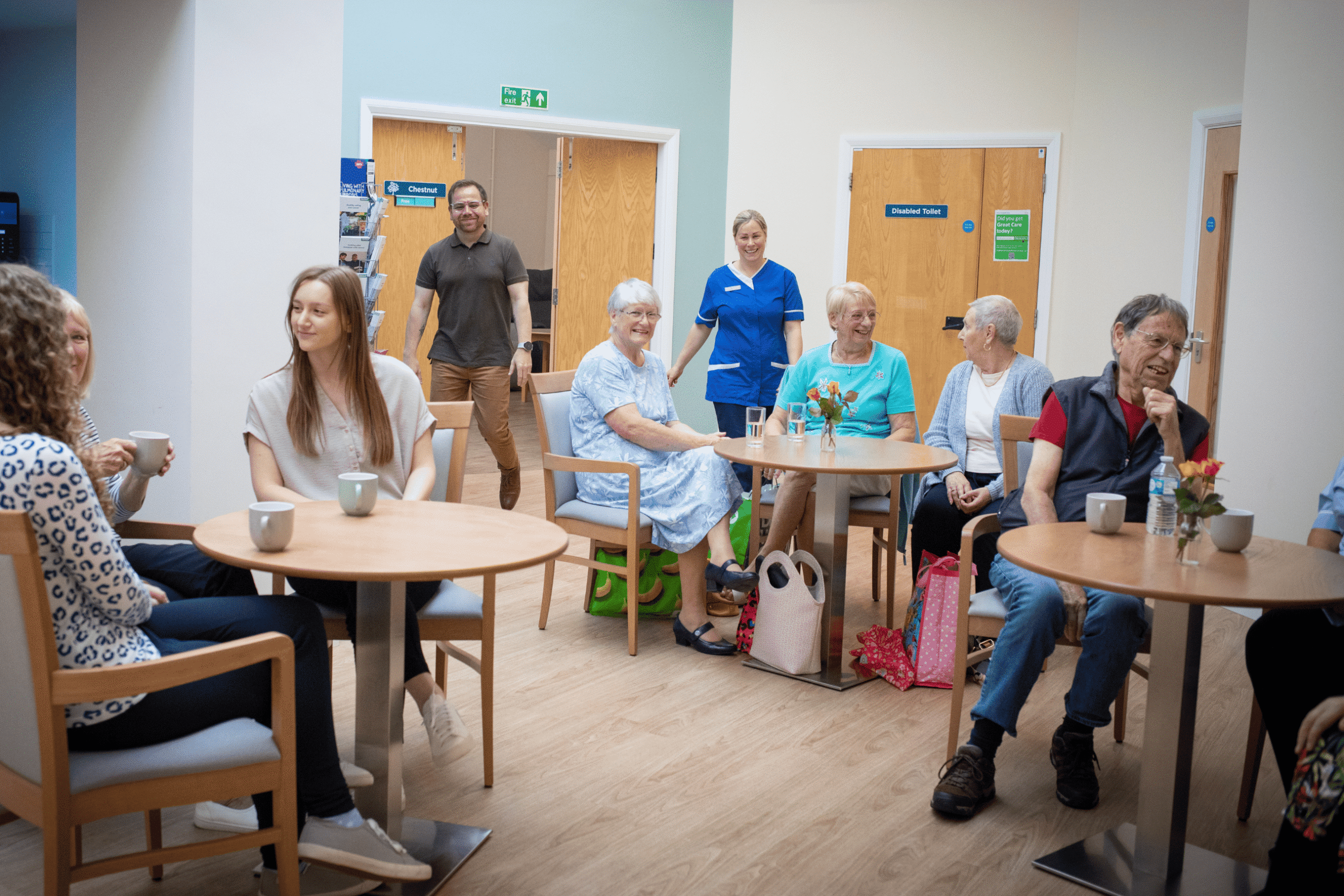 People of different ages sitting and standing in a light, airy room - all talking to one another.