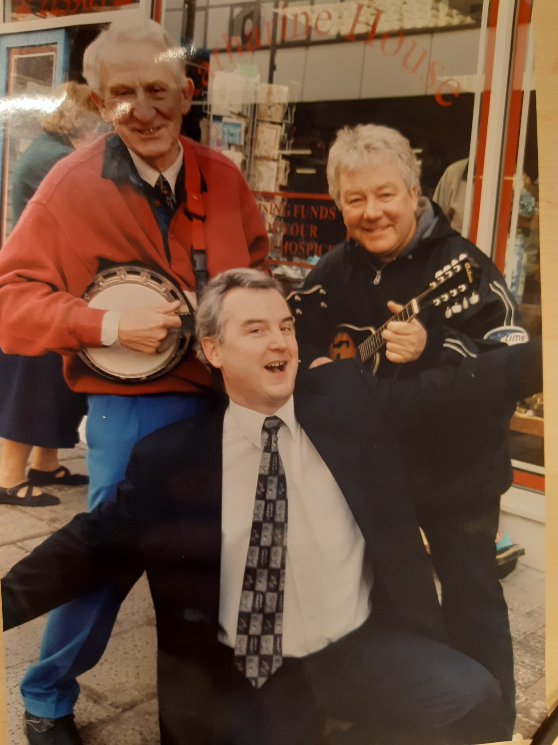 Richard smiling with his arms open wide and two men playing banjos
