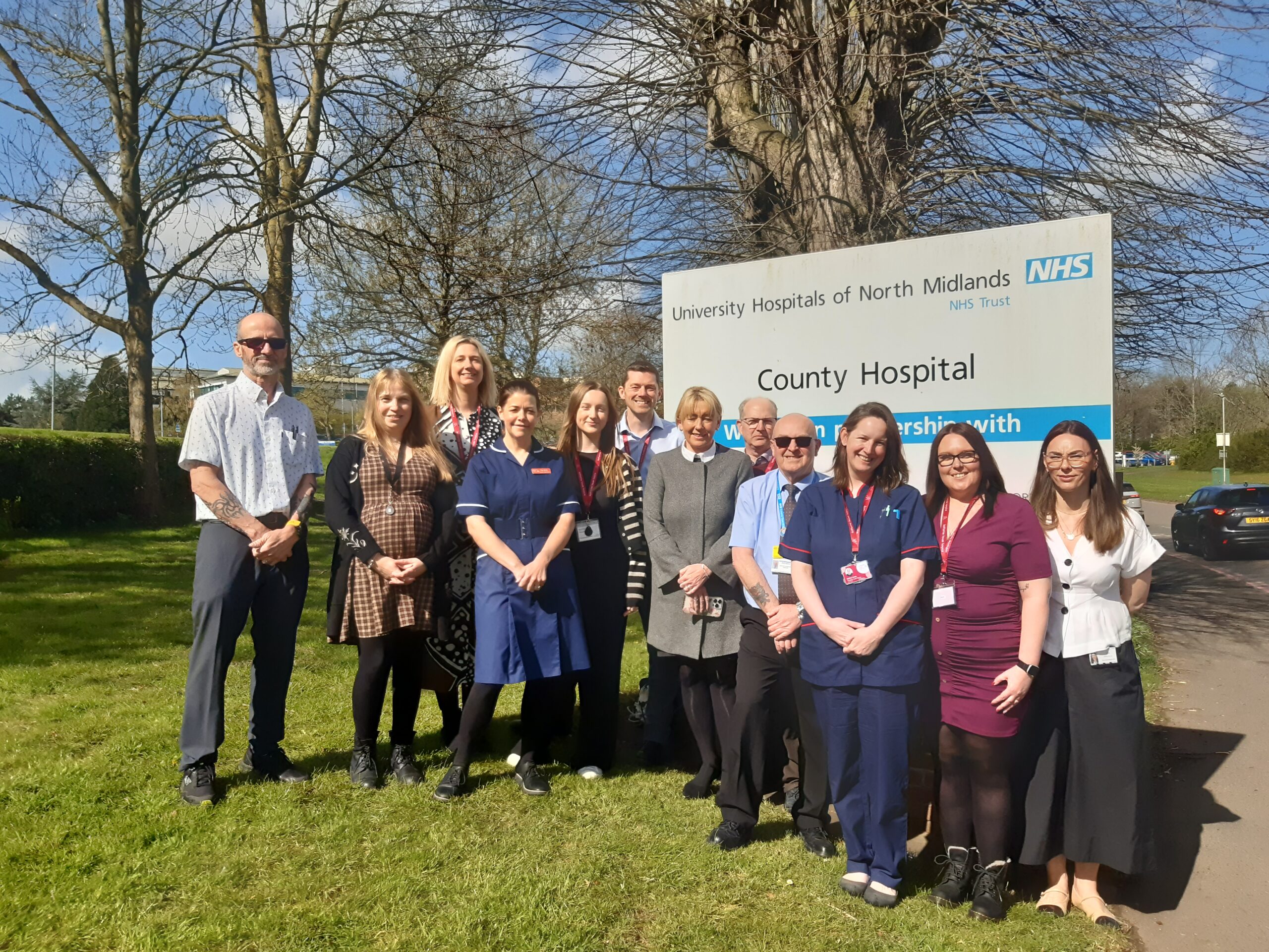 A group of people, some wearing nurses uniforms standing by the County Hospital sign