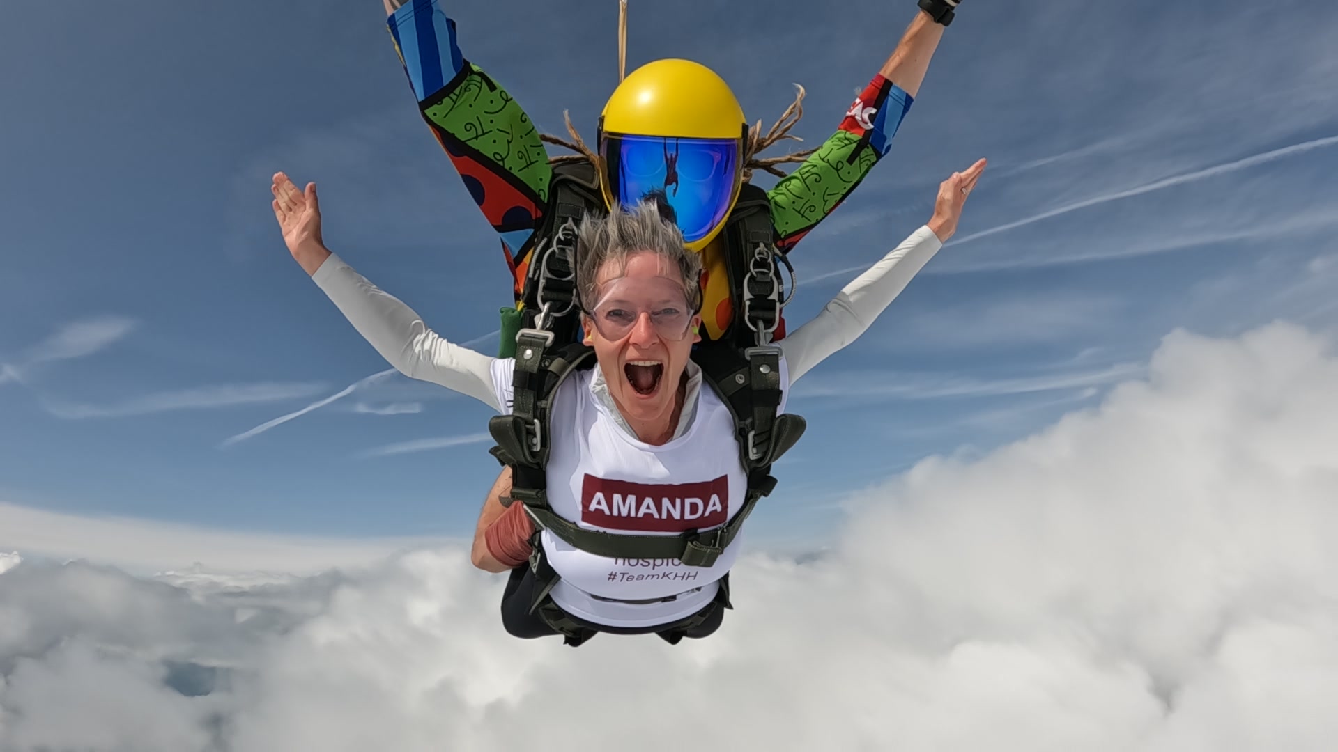 Amanda, manager of Extramile Digital, during her skydive for Katharine House Hospice. Shouting with joy, arms outstretched above a sea of clouds, with her instructor attached.