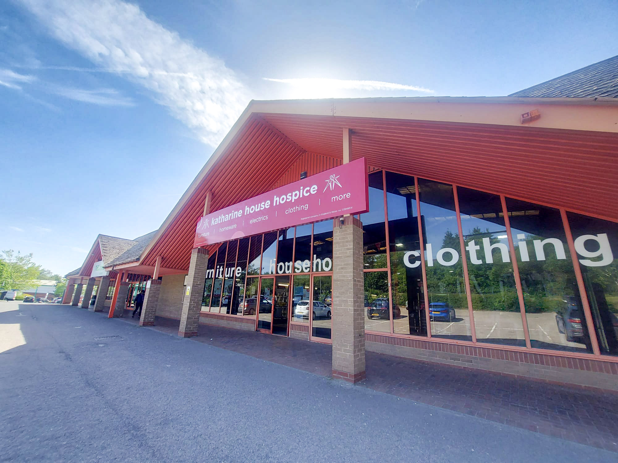 Sunlit Katharine House Hospice charity shop with red awning, large windows and a clear blue sky.