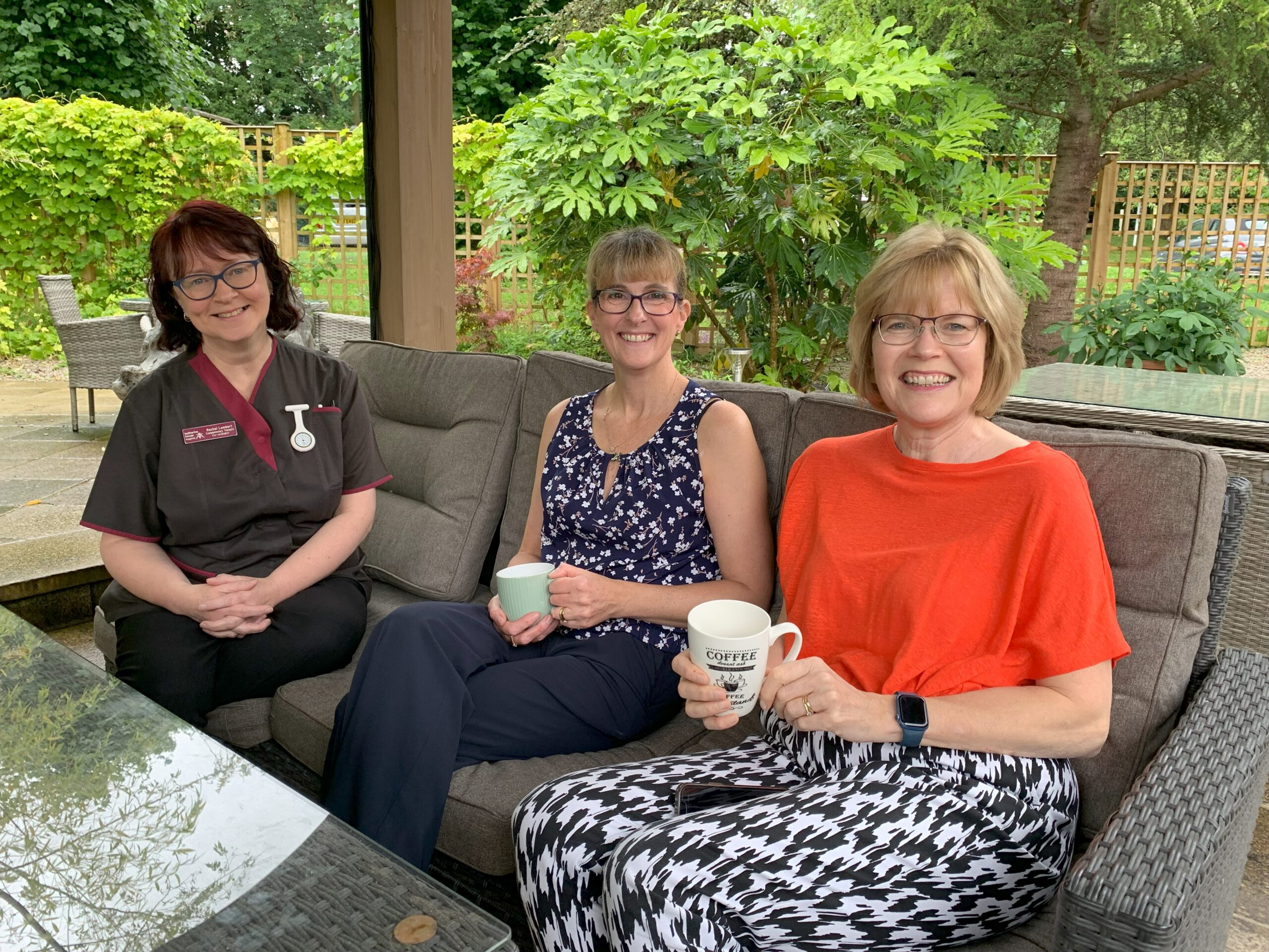 Three woman sat outside each holding a cup of tea and smiling.