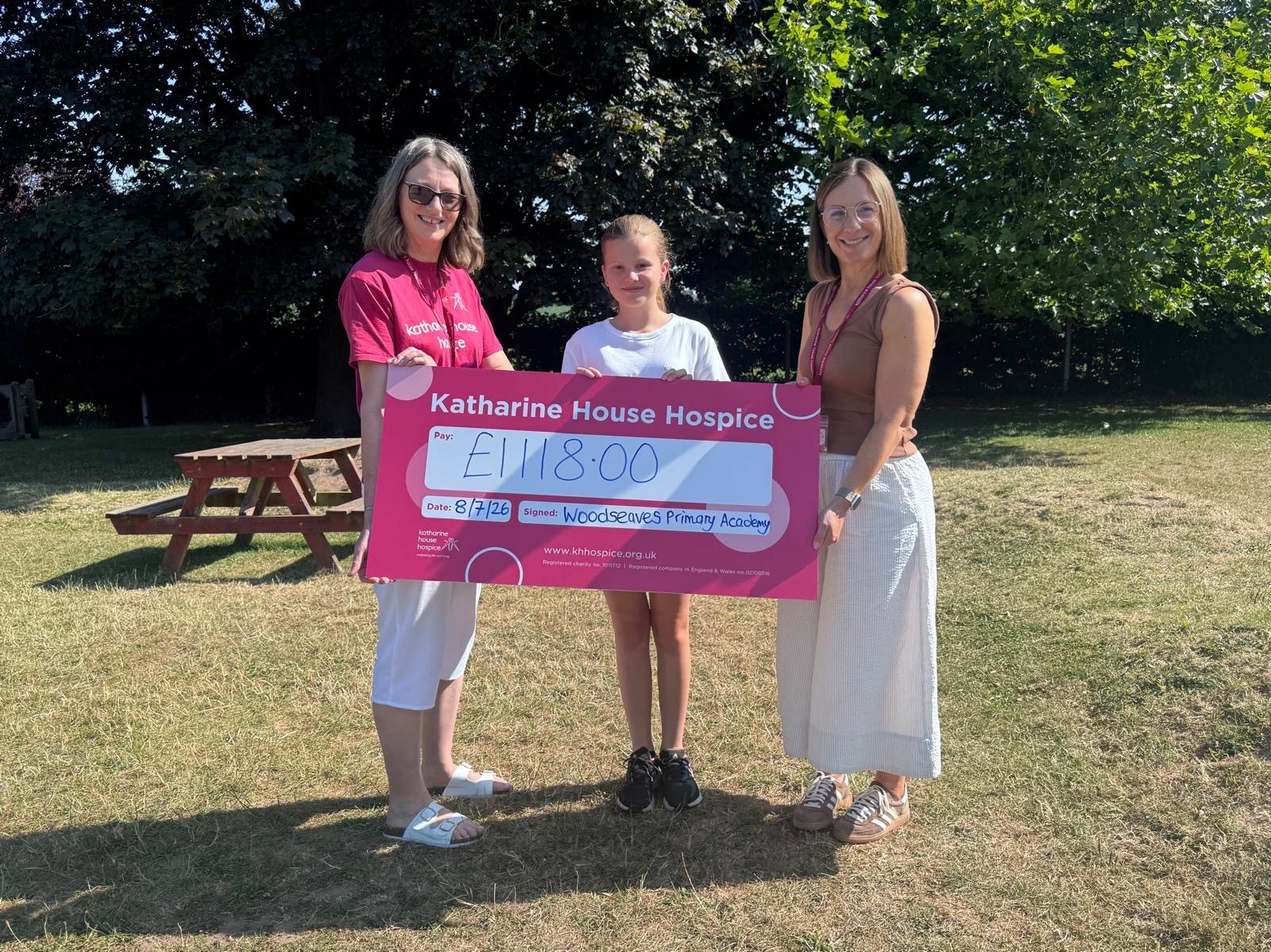 Two women and a young girl smiling as they hold a large cheque in support of Katharine House Hospice.