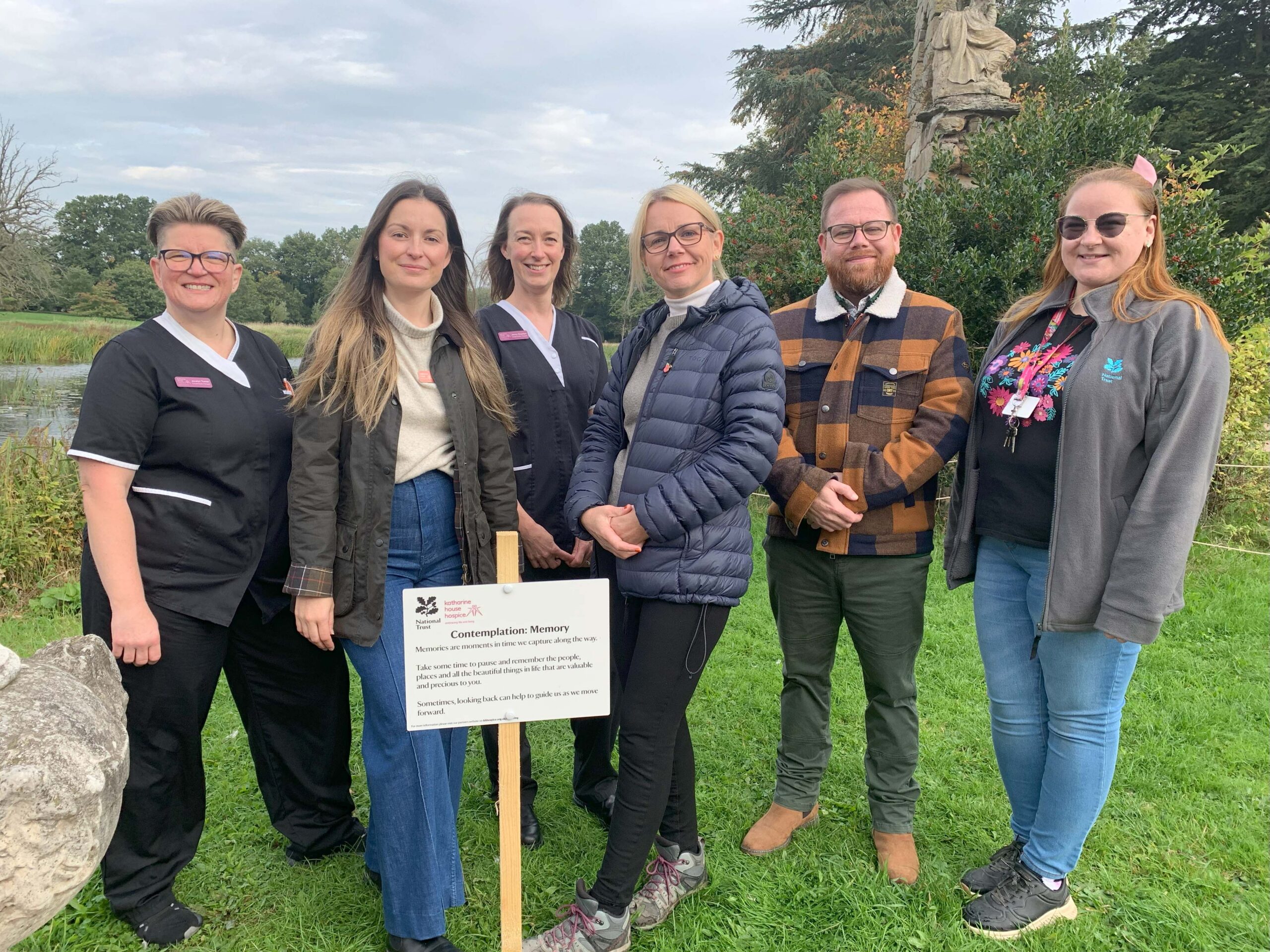 A group of people standing next to a wooden stake that encourages people to take time to pause, relfect and think of the things that are precious to them.