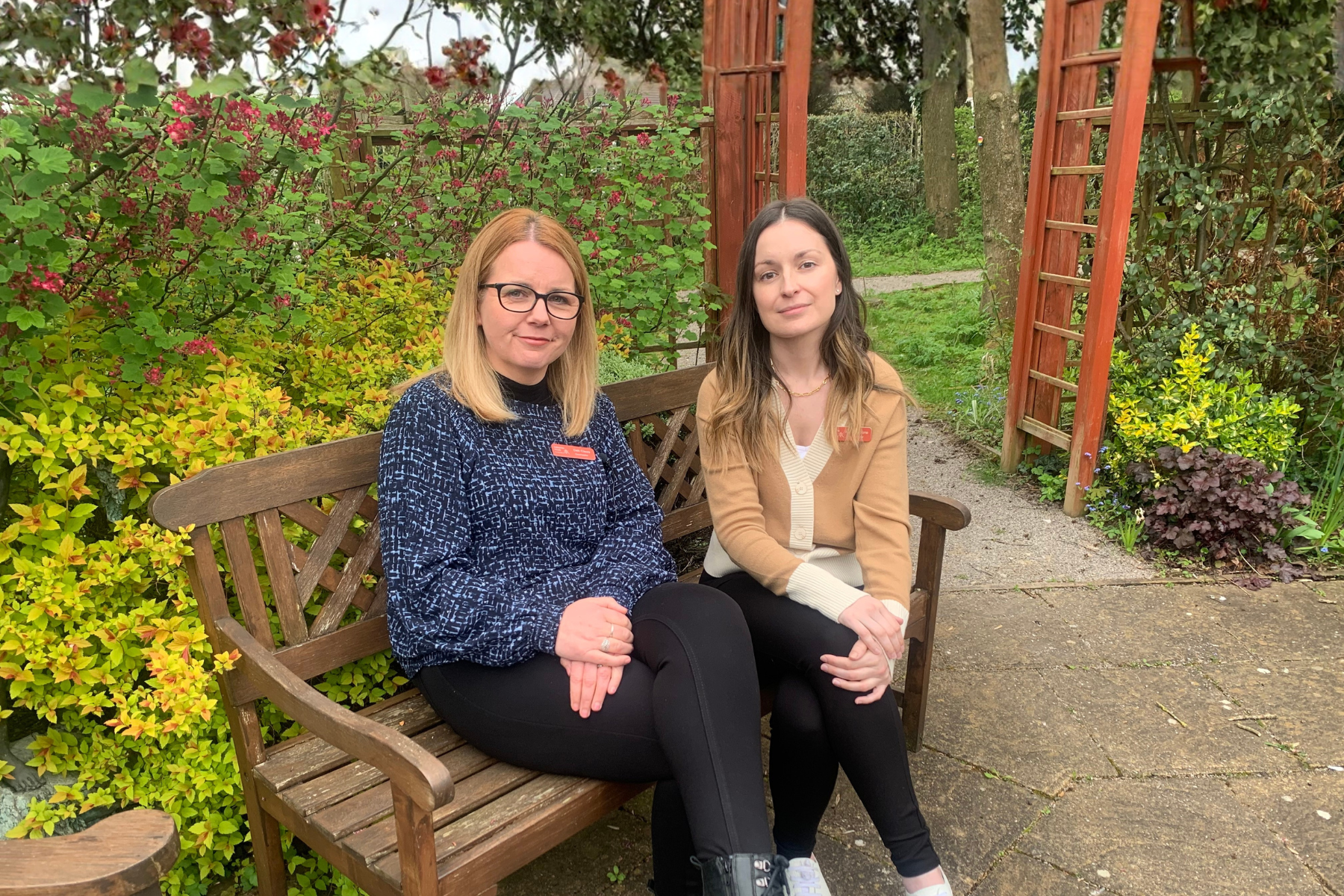Two women sitting on a bench in a garden.