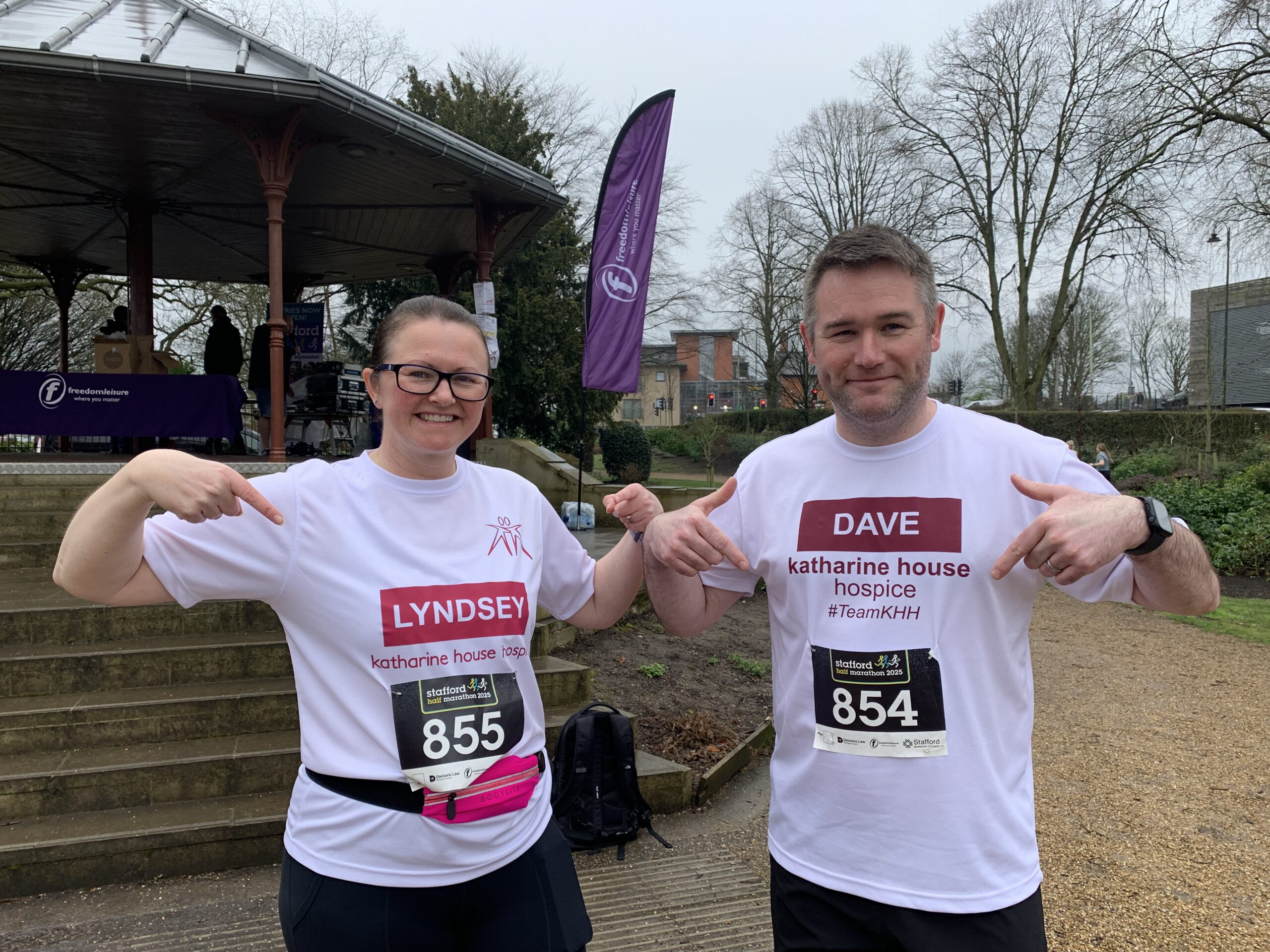 A man and woman pointing at their chest where there name is printed on their charity tops.