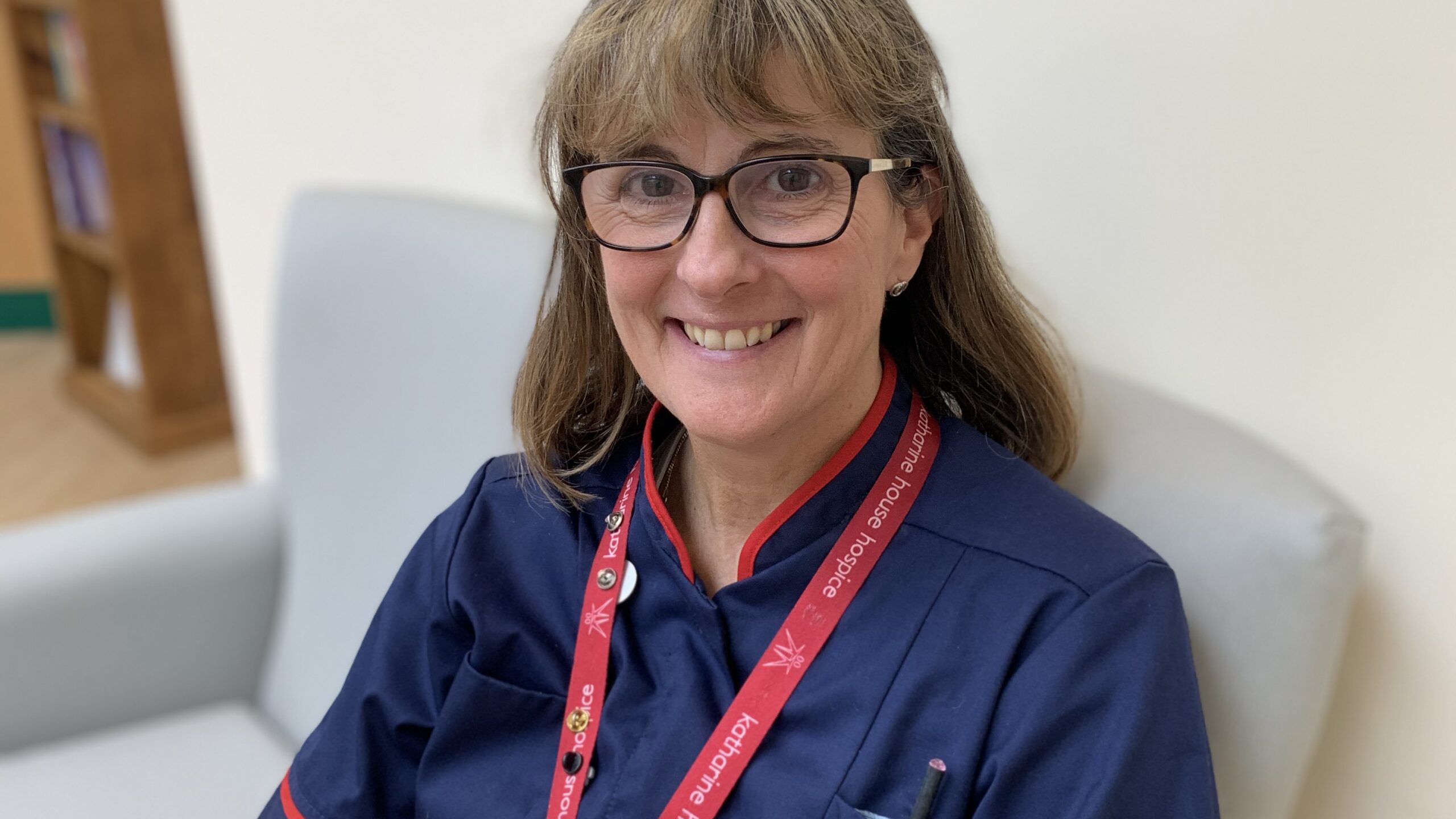 Cathy in her blue nurses uniform sitting on a chair in Therapy & Wellbeing