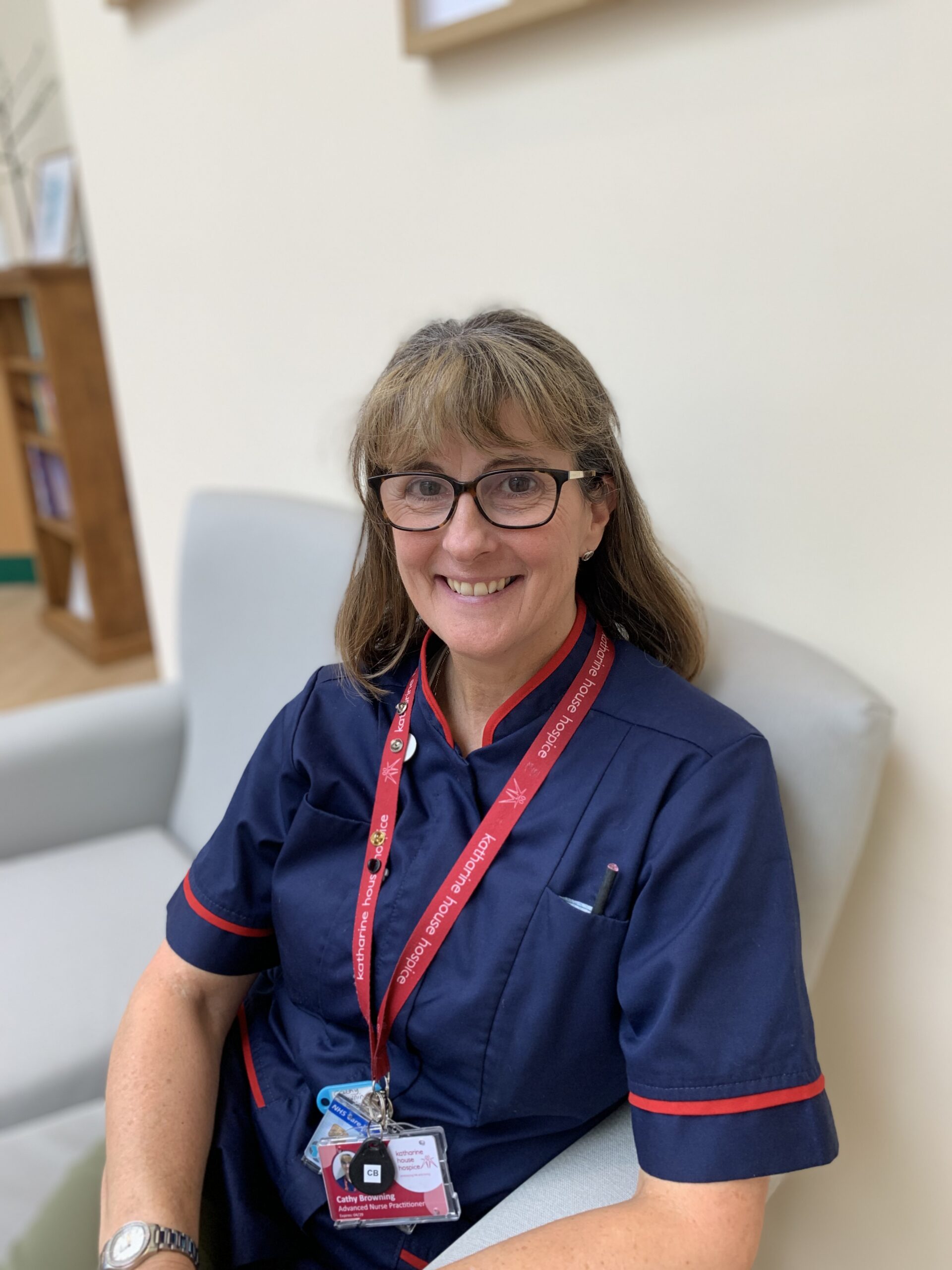 Cathy in her blue nurses uniform sitting on a chair in Therapy & Wellbeing