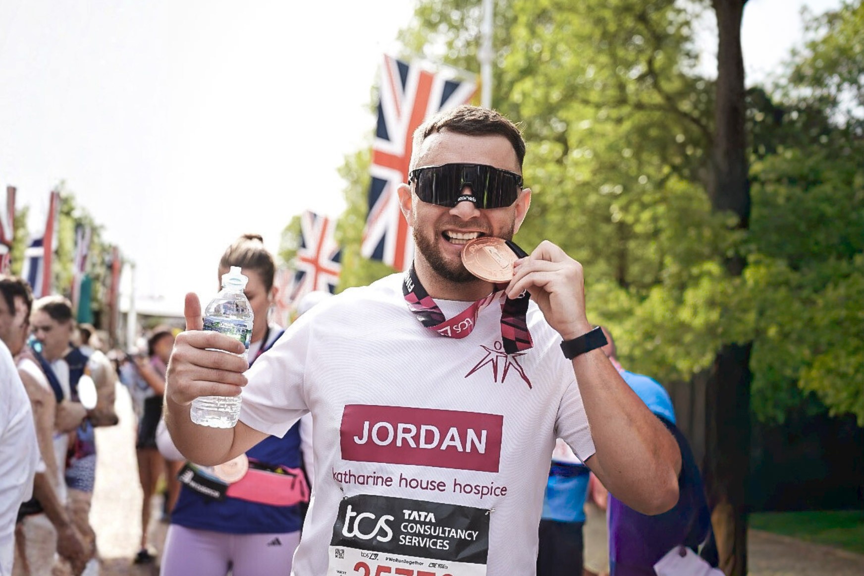 A runner wearing a Katharine House Hospice top bites his London Marathon medal celebrating.