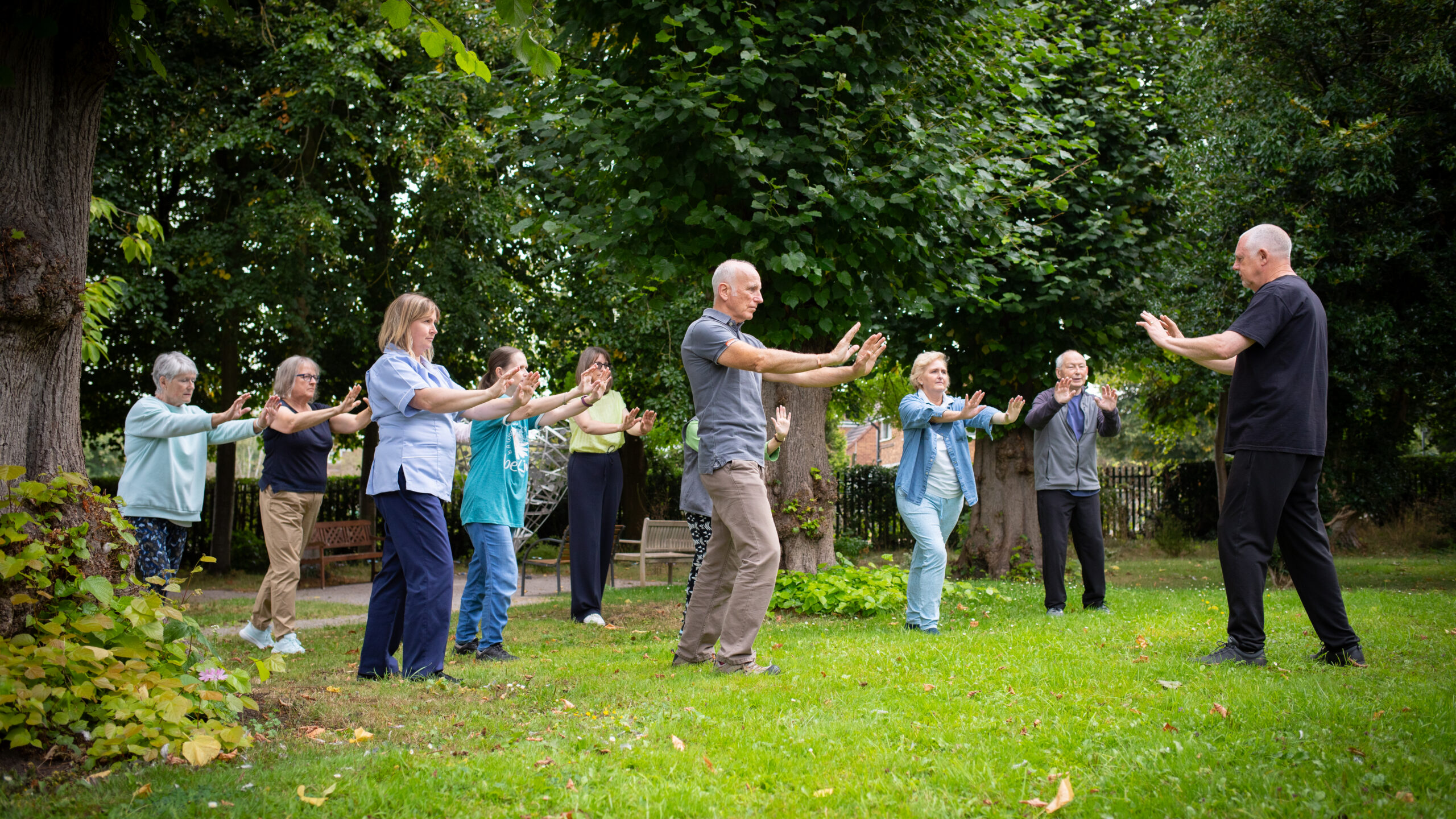 A group of people doing tai chi outside on the grass on a sunny day.