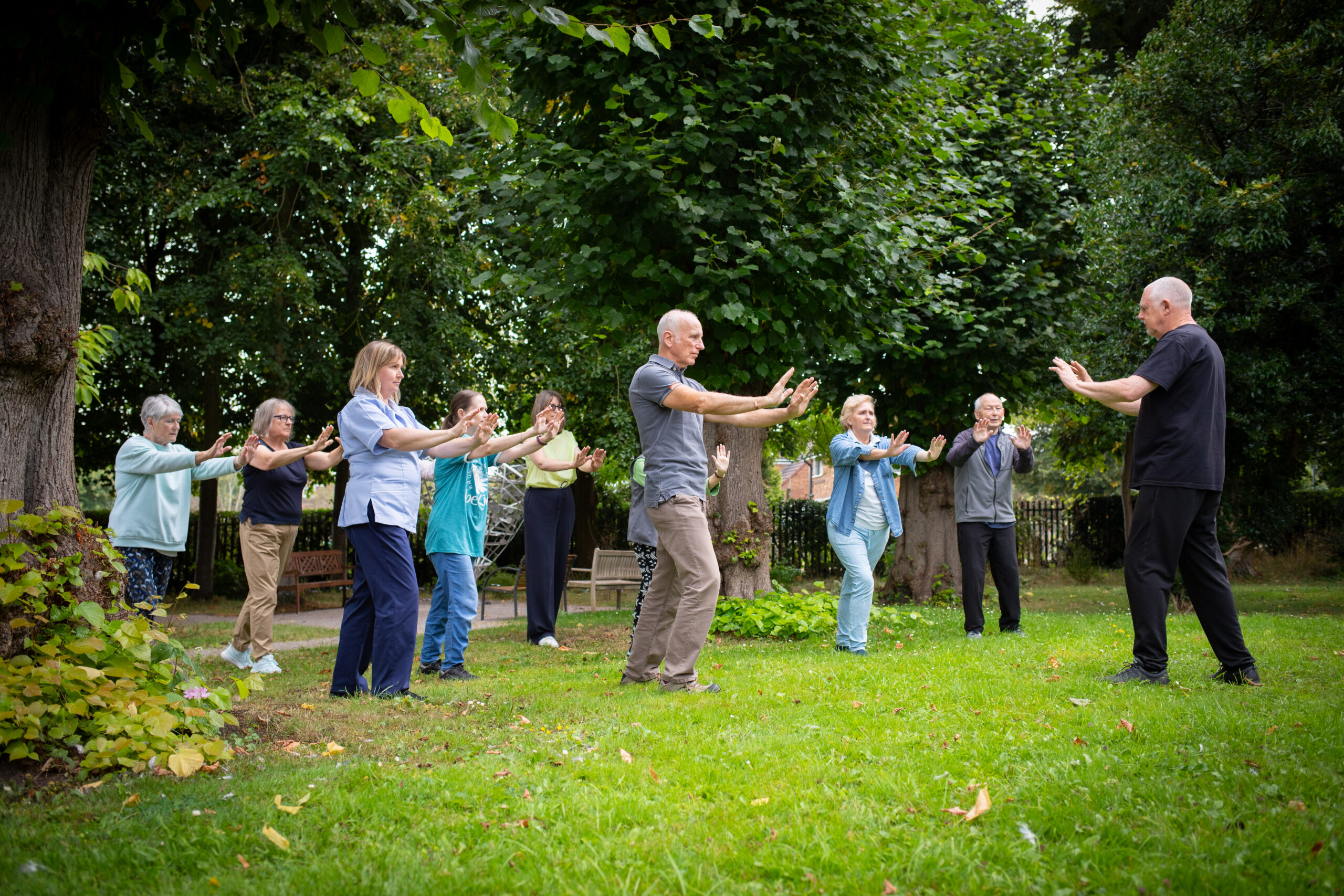 A group of people doing tai chi outside on the grass on a sunny day.