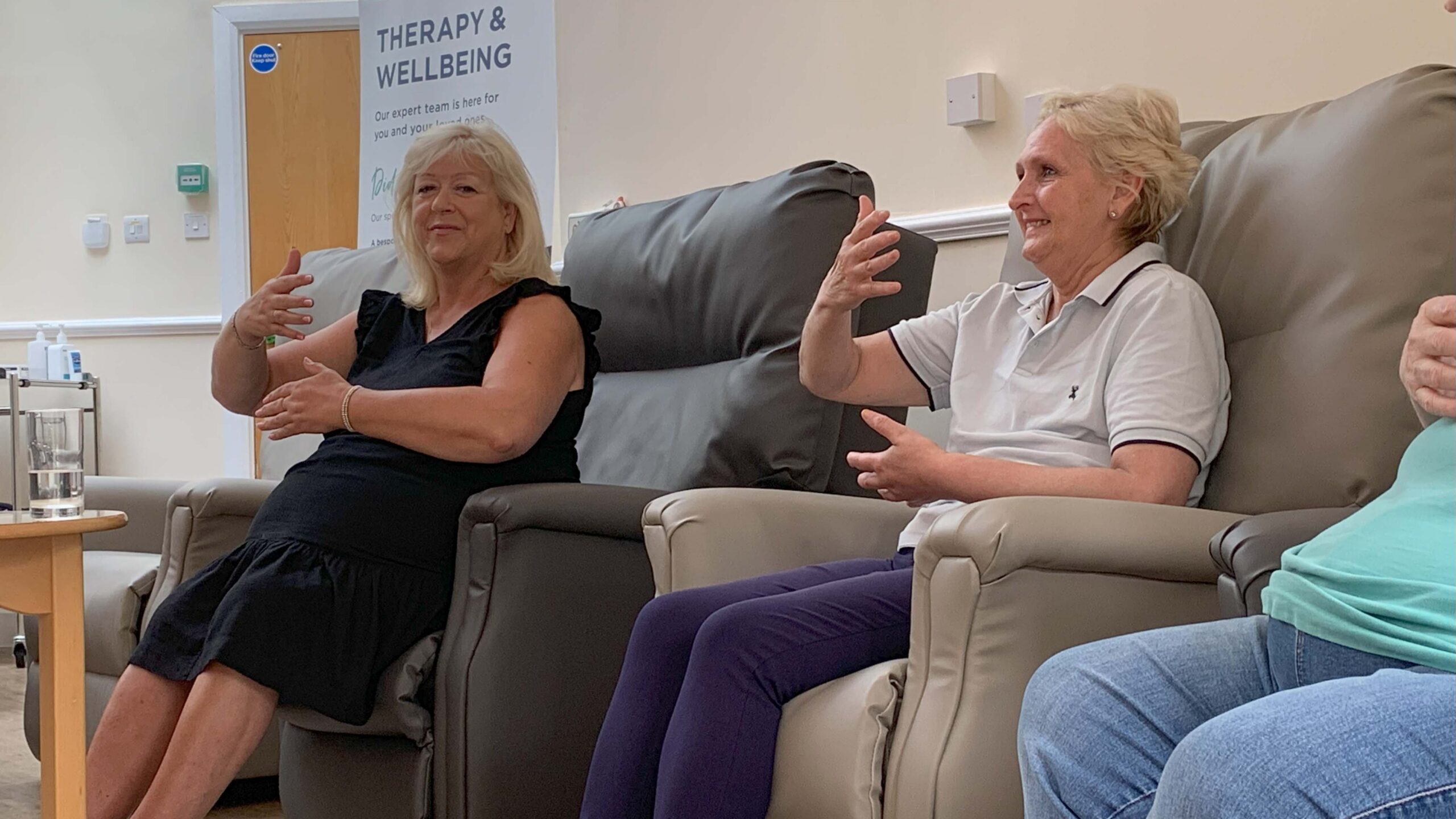 Close up of two people sitting down in a calm room, using their arms to perform a tai chi movement.