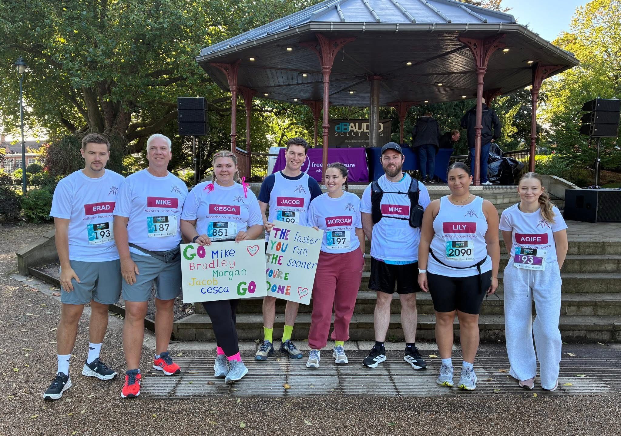 eight people wearing running gear and Katharine House Hospice t-shirts standing in front of a bandstand in Victoria Park