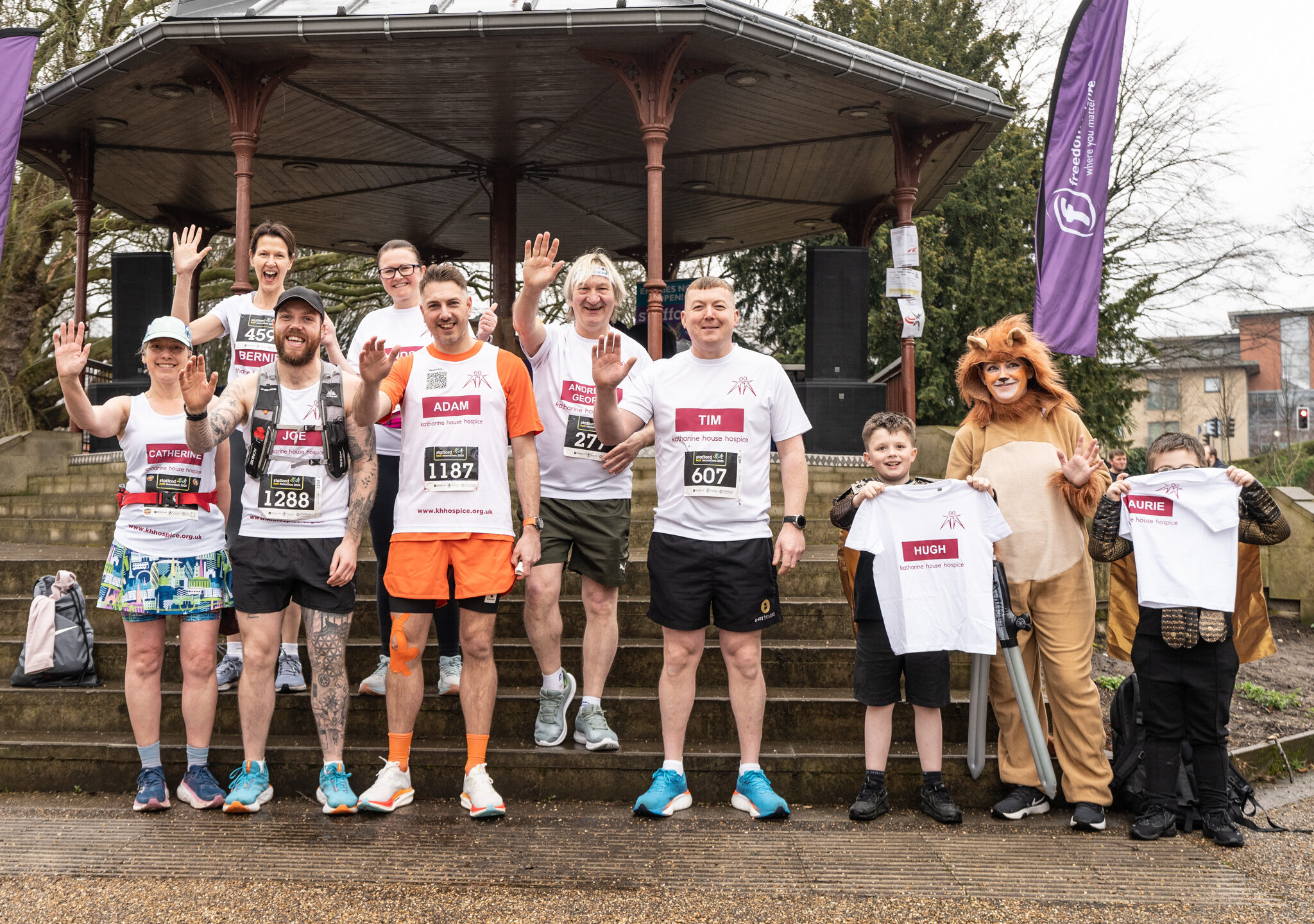 Adults and children waving, wearing Katharine House Hospice running tops before the race.