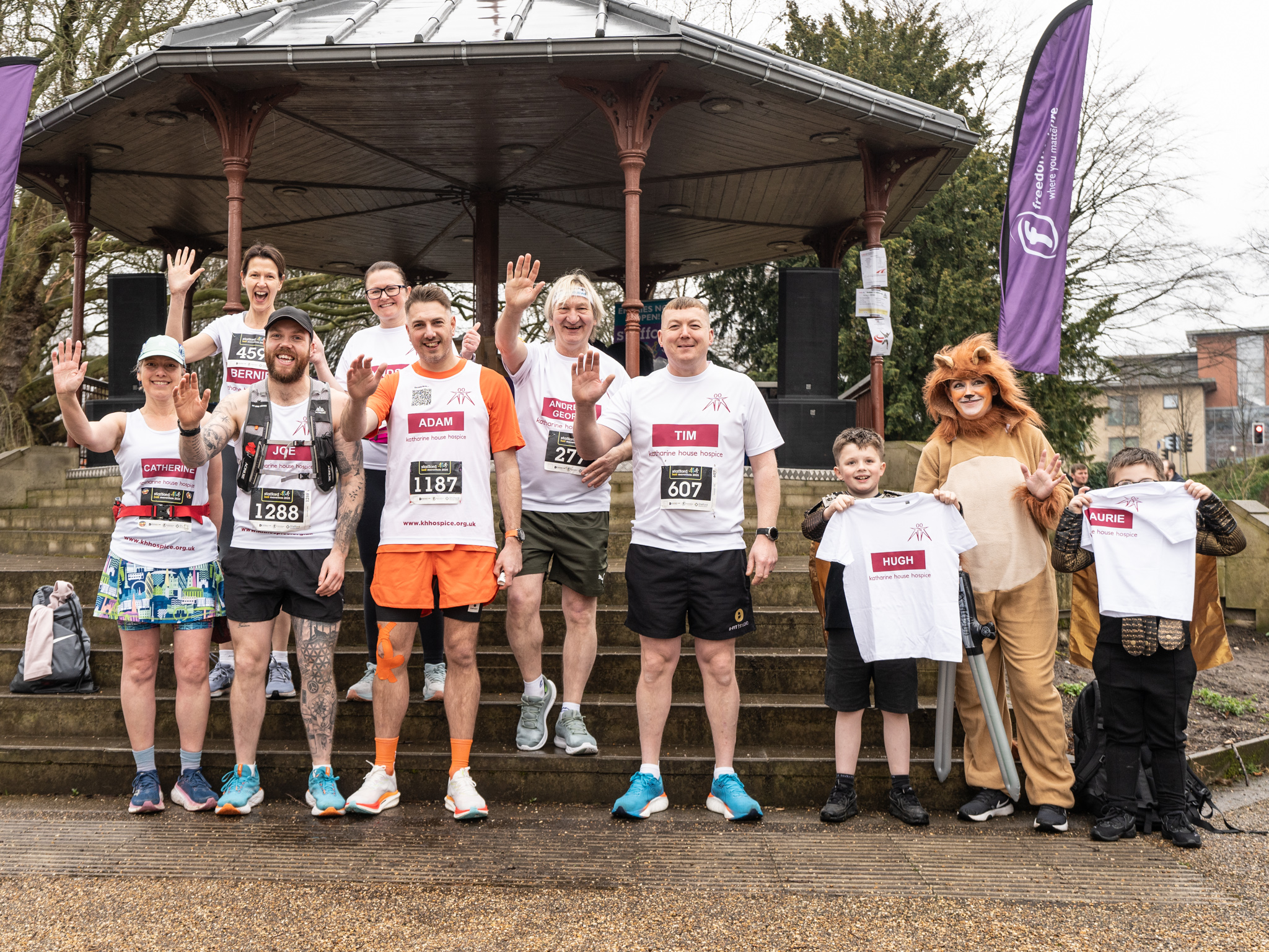 Adults and children waving, wearing Katharine House Hospice running tops before the race.