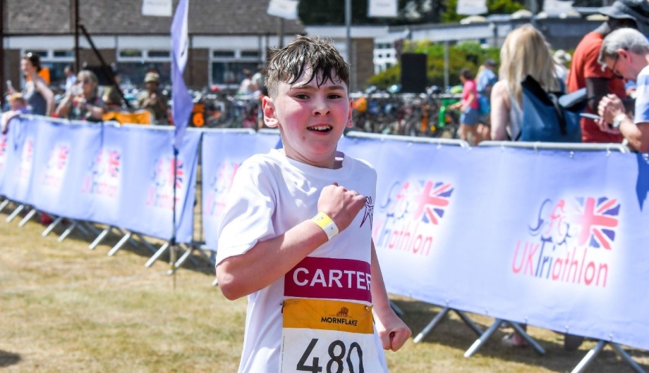Young male triathlon participant running while smiling at the camera. He is wearing a Katharine House Hospice T-shirt.