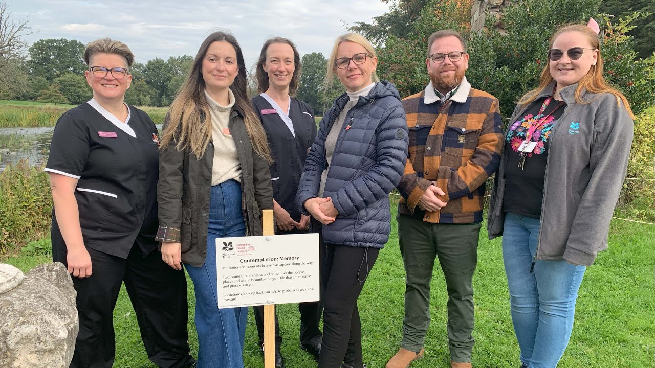 A group of people standing next to a wooden stake that encourages people to take time to pause, relfect and think of the things that are precious to them.