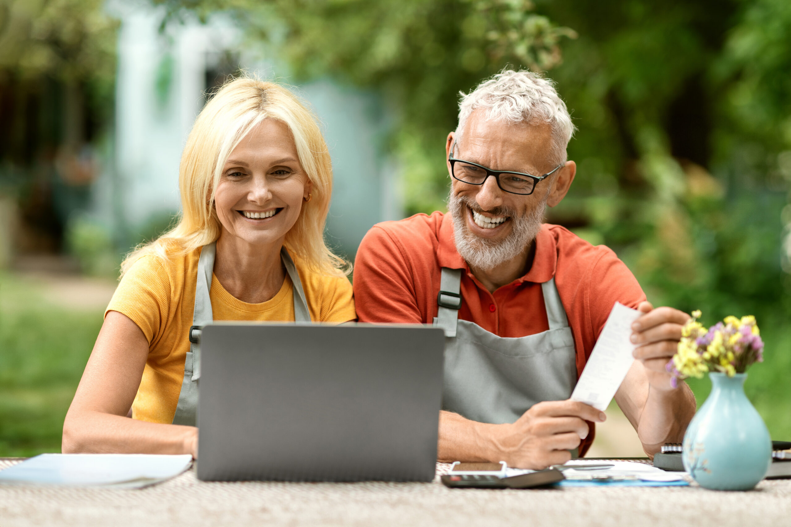 Portrait of happy senior couple using laptop outdoors in their garden.