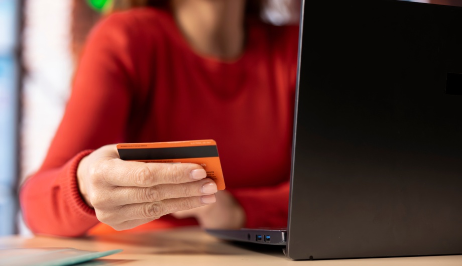 Close-up of a person holding a bank card in front of a laptop while making a donation online.