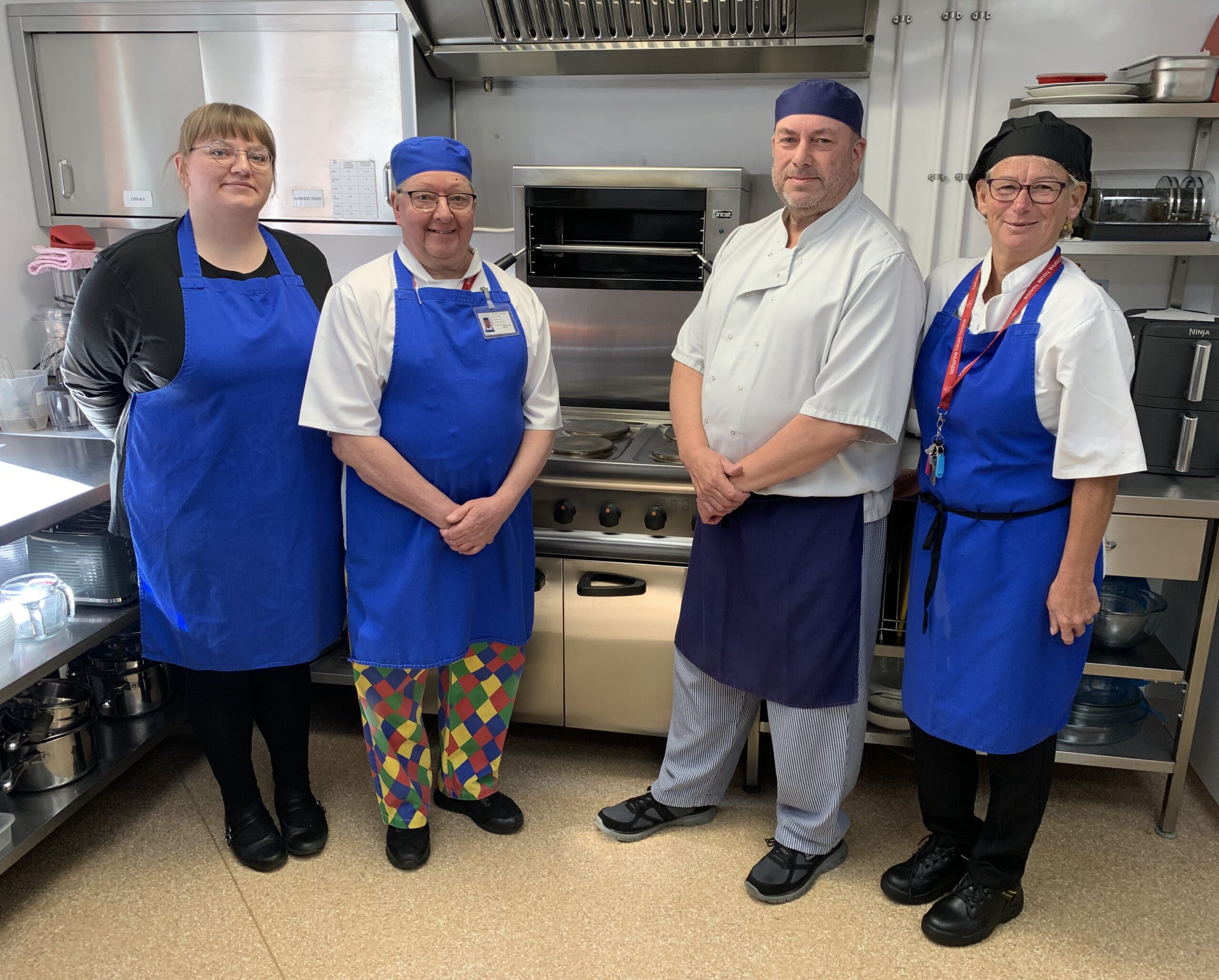 Four members of the hospice kitchen team wearing aprons and standing together in the kitchen.