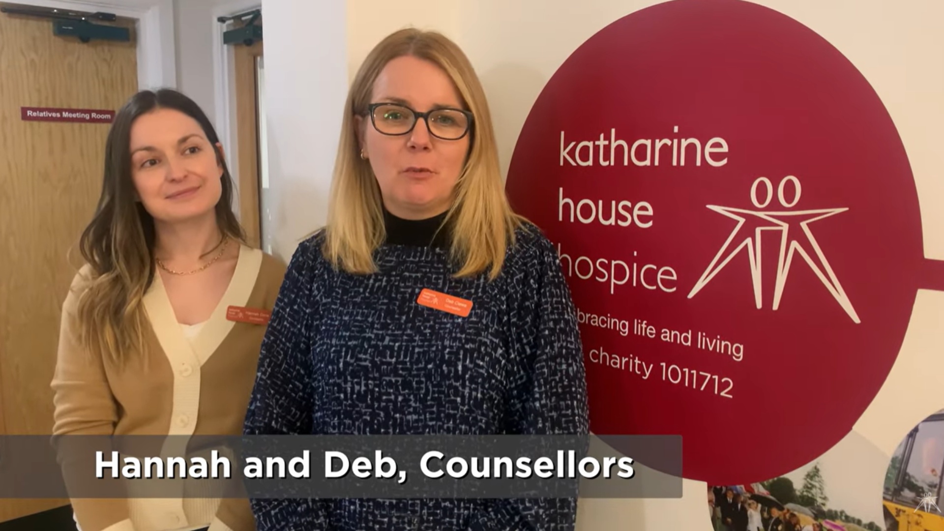 Two female members of staff stand beside a Katharine House Hospice display banner inside the hospice.