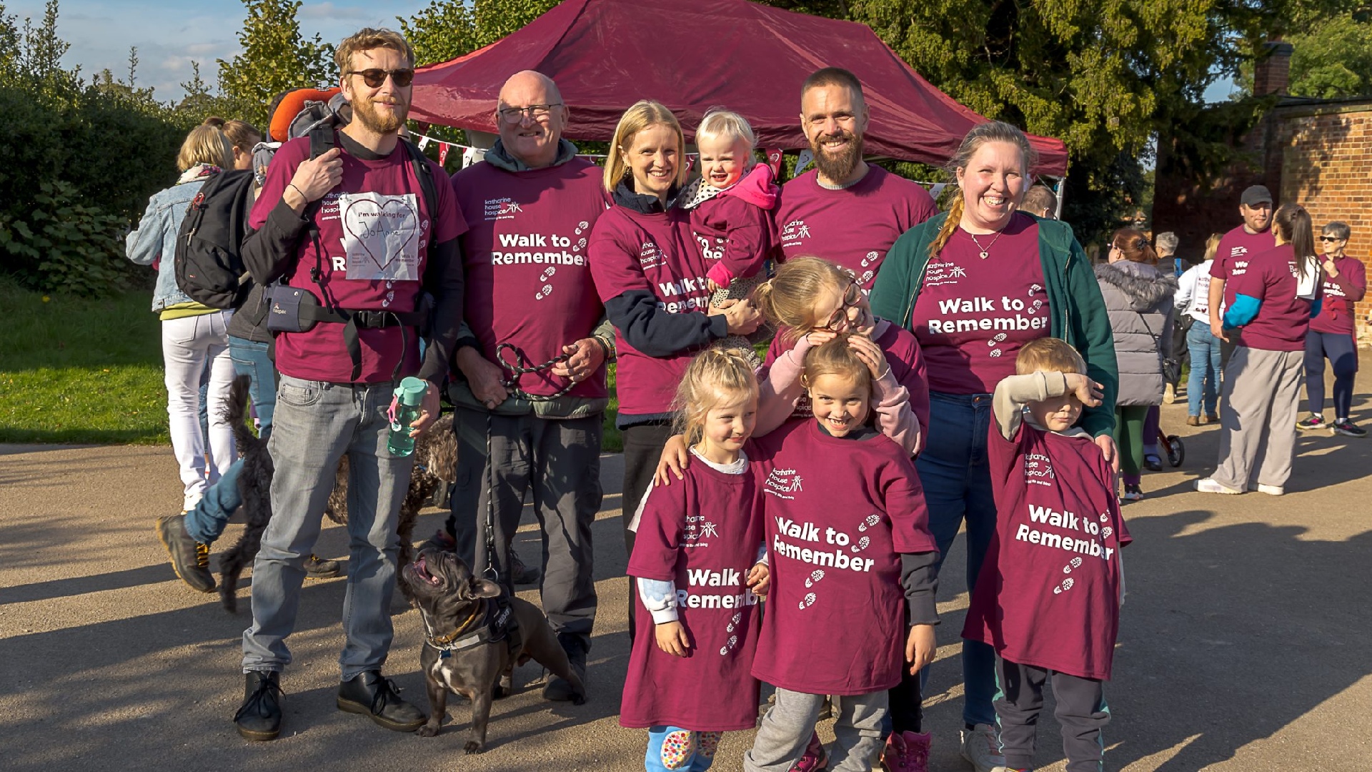 Multigenerational family (and dog) wearing Katharine House Hospice Walk to Remember event T-shirts and smiling at the camera.