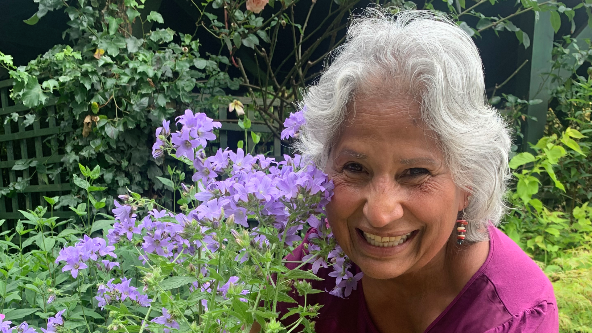 Smiling lady among purple flowers in a garden.