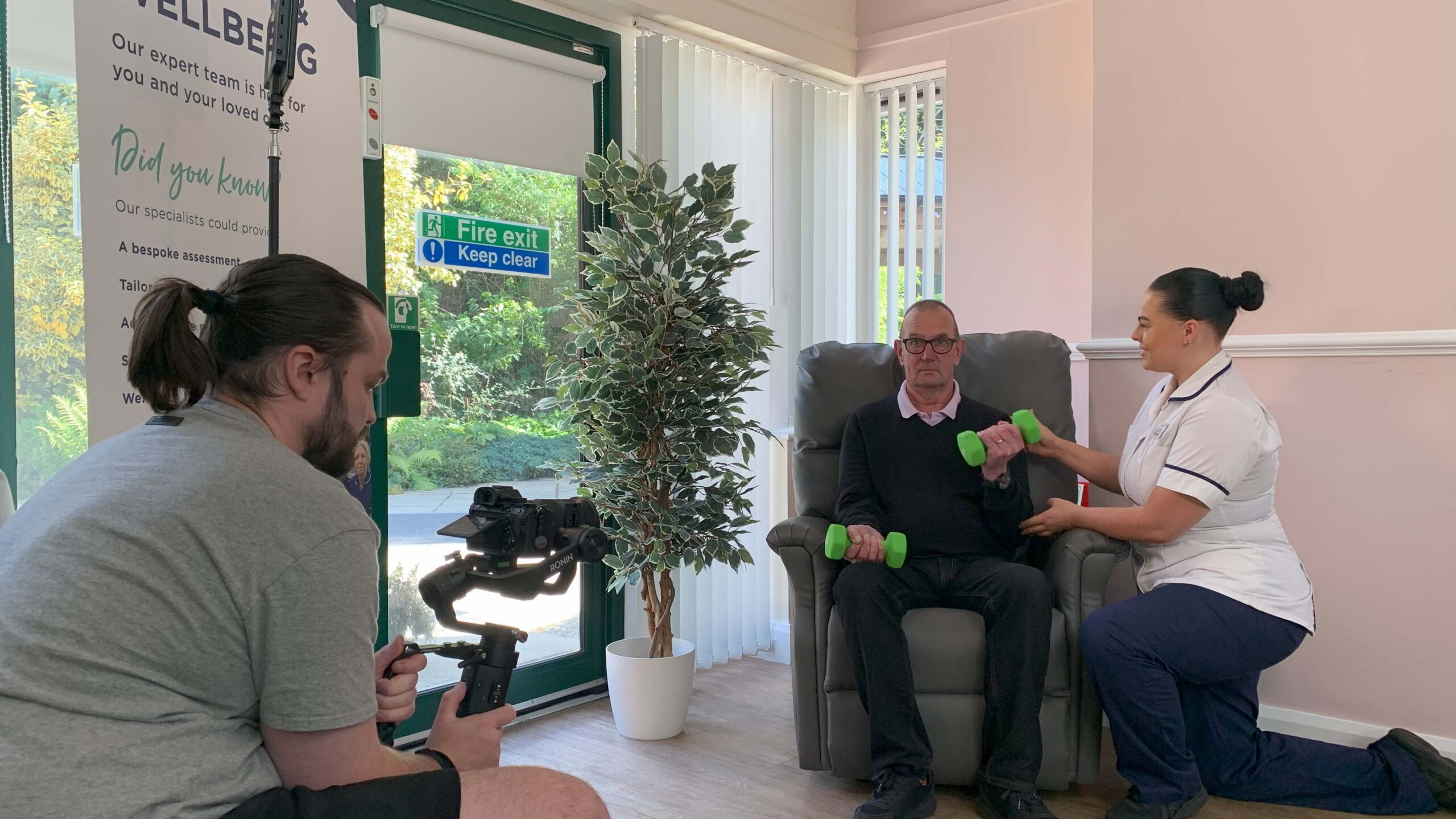 A man crouched down, filming a physio working with a patient.