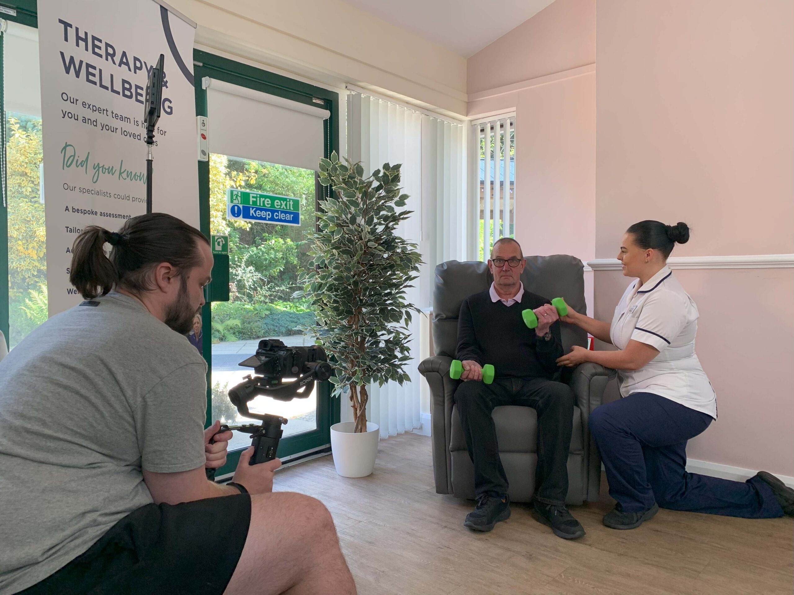 A man crouched down, filming a physio working with a patient.