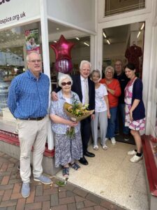 A 90-year-old woman holds a large bouquet of flowers, surrounded by staff members.